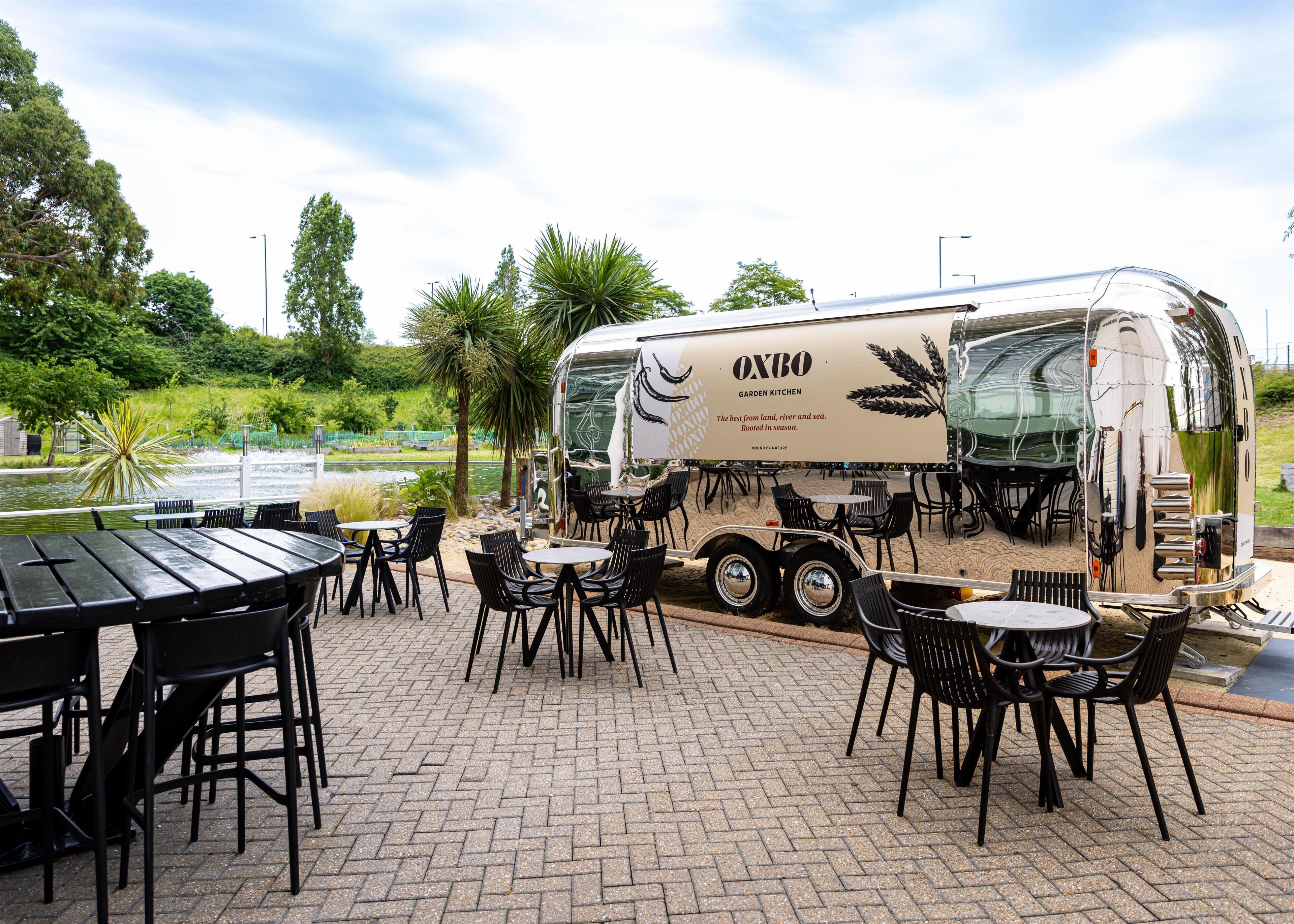 A garden kitchen trailer with outdoor seating and a view of a water body.