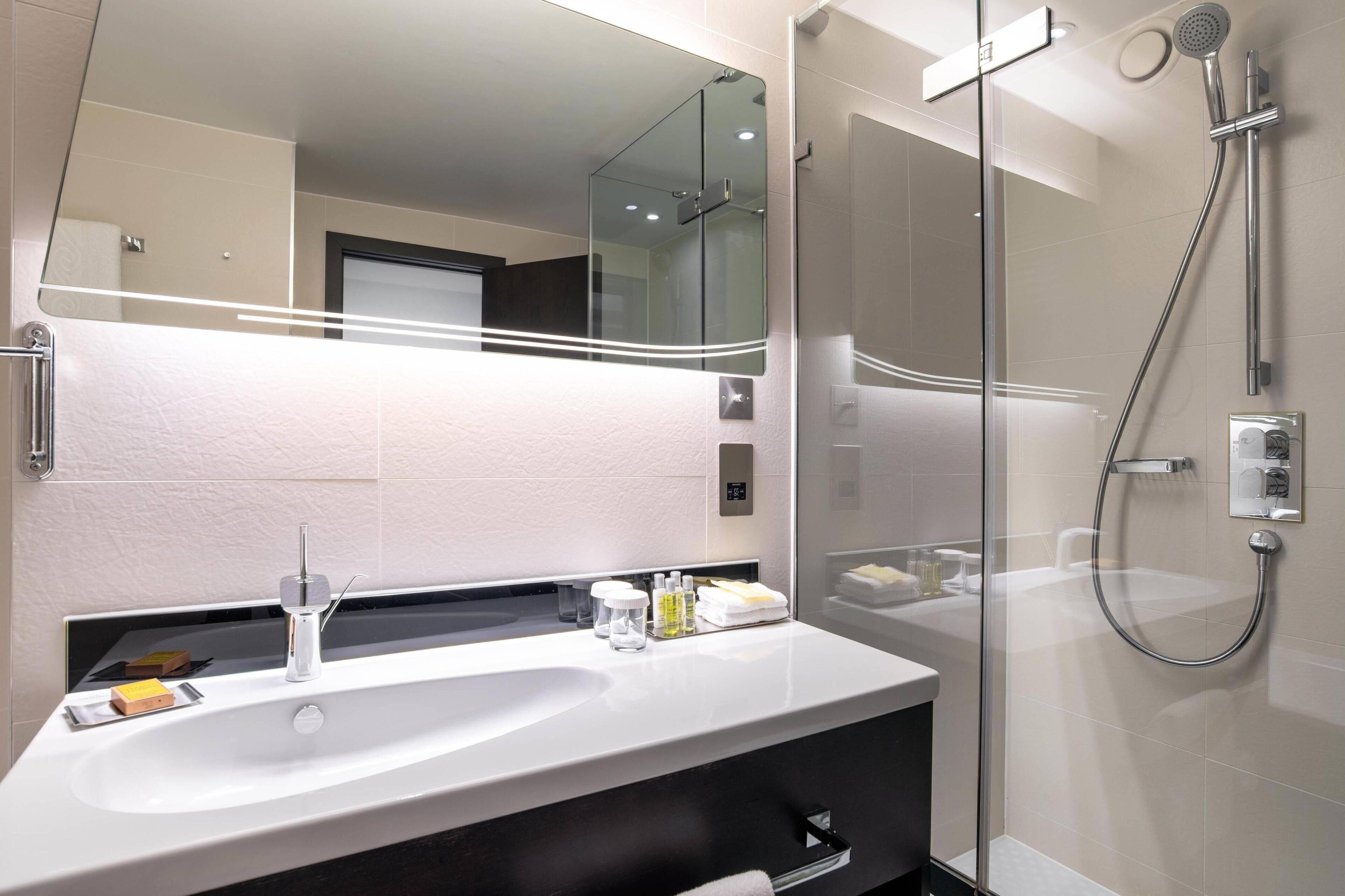 A modern bathroom with a large mirror, a sink, and a shower.