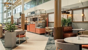 A spacious indoor area with high ceilings, large windows, and a variety of seating arrangements including tables and chairs. - Hilton London Heathrow Airport Hotel (Hounslow)