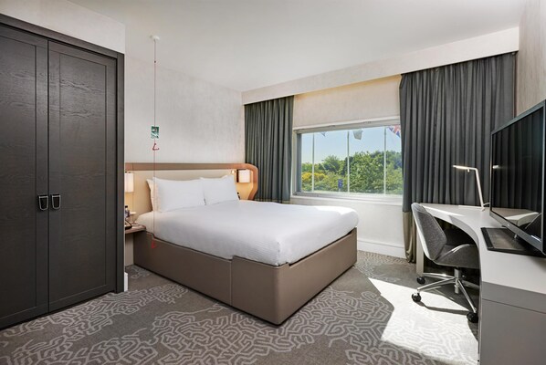 A hotel room with a bed, desk, and wardrobe.