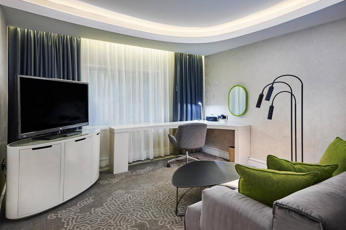 Hotellihuone, jossa on taulutelevisio, työpöytä, tuoli, sohva ja peili.