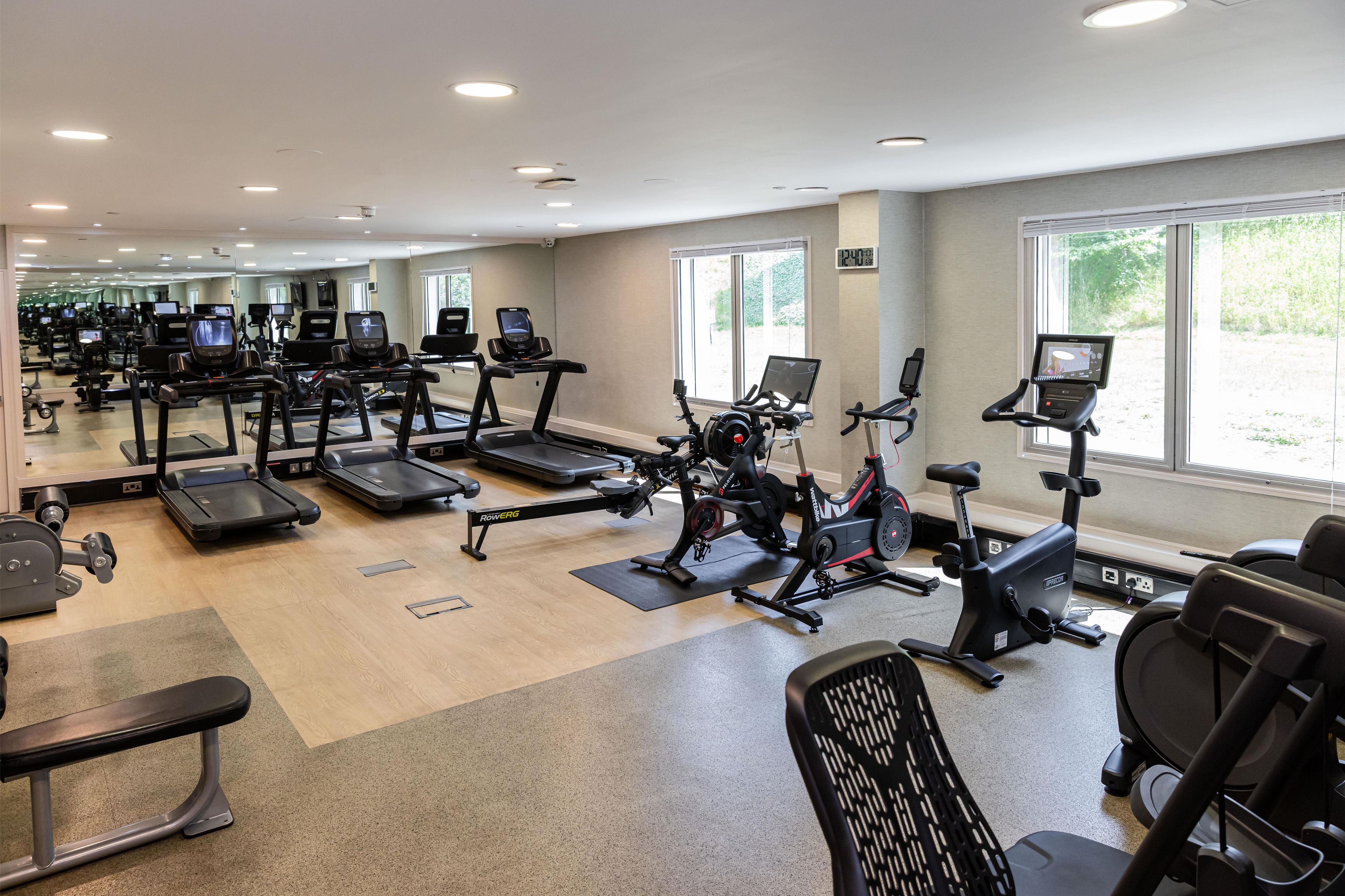 A gym with various exercise machines, mirrors, and large windows.