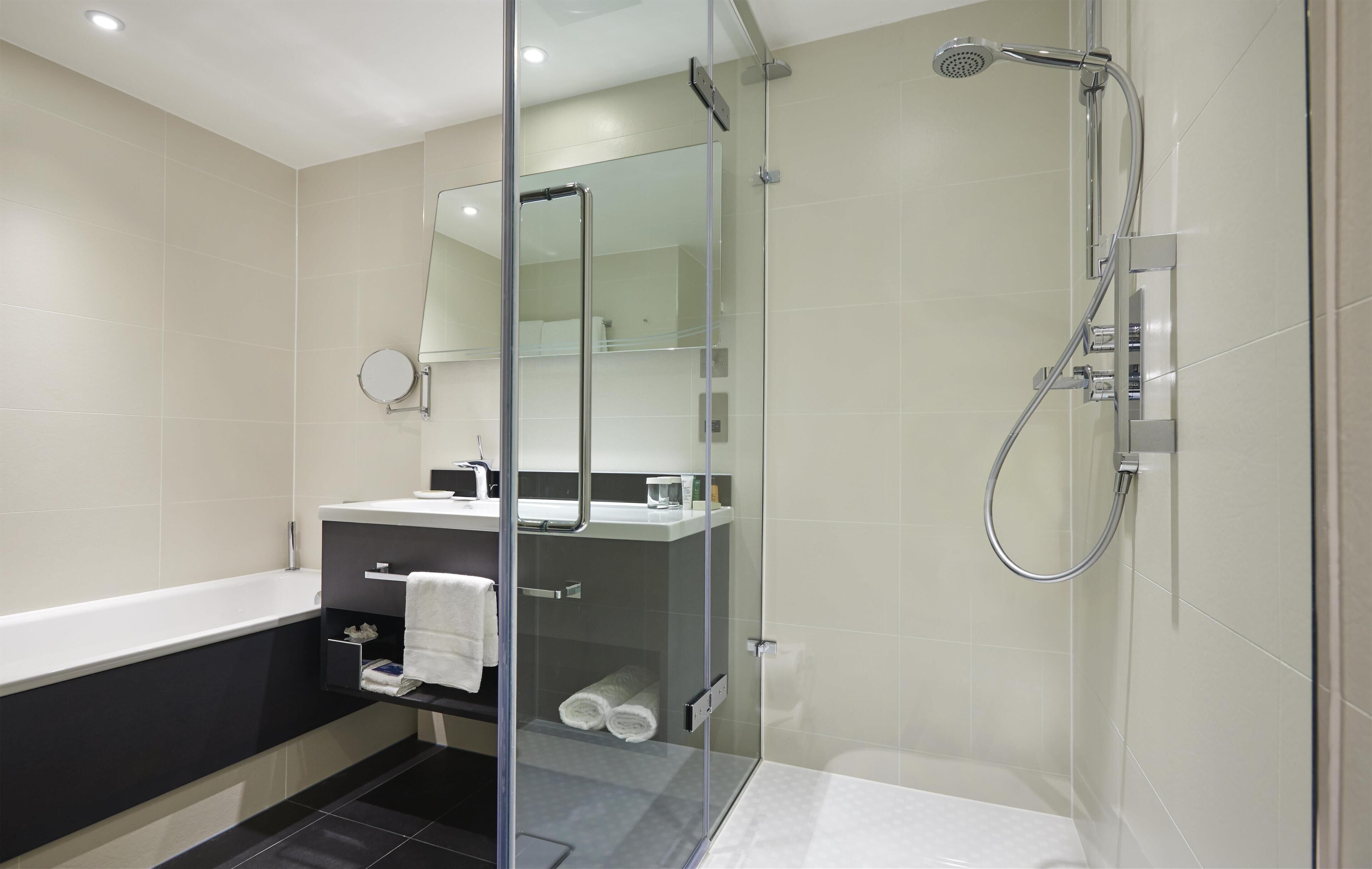 A modern bathroom with a glass-enclosed shower, a separate bathtub, and a vanity with a mirror.