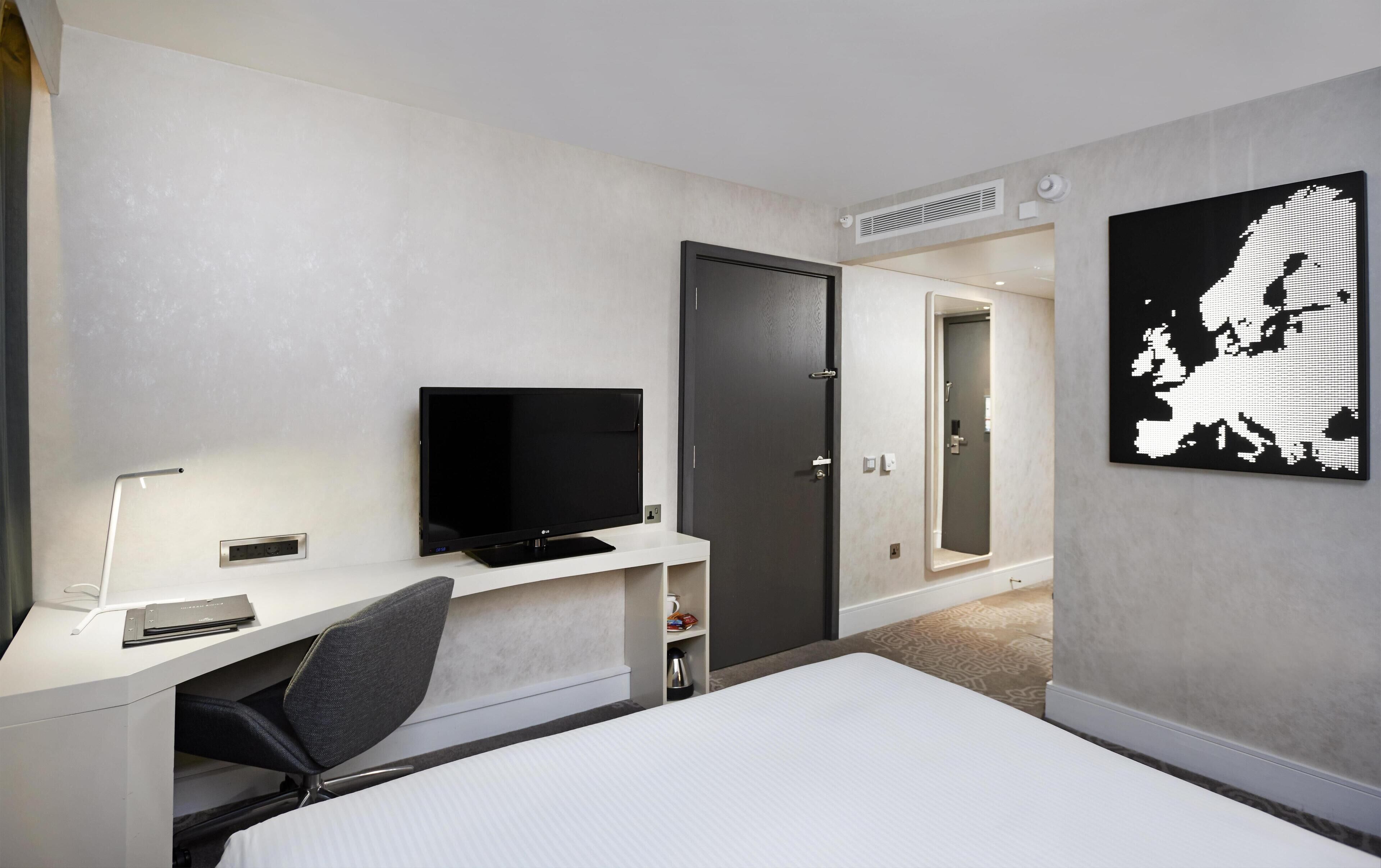 A hotel room with a bed, a TV, a desk, a chair, a wardrobe, and a mirror.