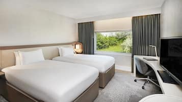 A hotel room with two beds, a desk, a TV, and a window with curtains.