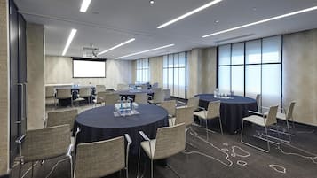 A conference room with multiple tables, chairs, and a projector screen.
