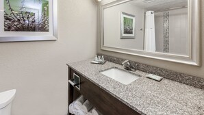 Une salle de bain avec un lavabo doté d’un plan de travail en granit, un grand miroir et un tableau encadré au mur.