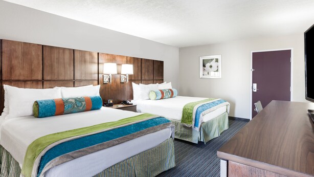 Une chambre d’hôtel avec deux lits, une tête de lit en bois, un bureau et un téléviseur.