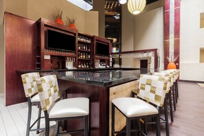 Un espace bar comprenant un comptoir, des tabourets de bar et des étagères remplies de bouteilles.