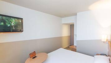 Une chambre d’hôtel avec un lit, une petite table avec un téléphone, un téléviseur fixé au mur et un miroir avec un éclairage intégré.