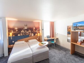A hotel room with a bed, a desk, a chair, a television, and a cityscape mural on the wall. - ibis Styles Angers Centre Gare (Angers)
