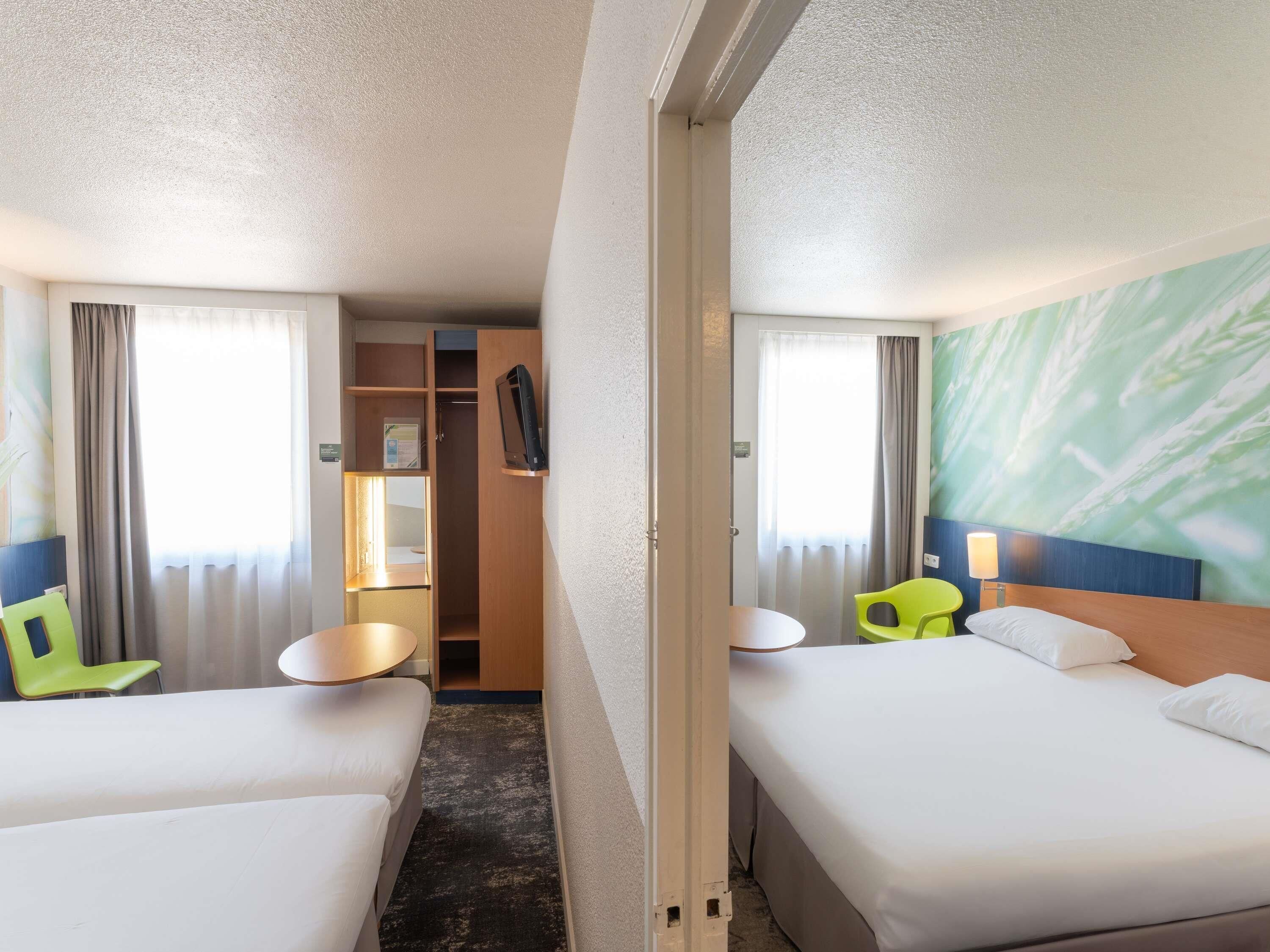 A hotel room with two beds, a desk, a chair, a wardrobe, and a bathroom.