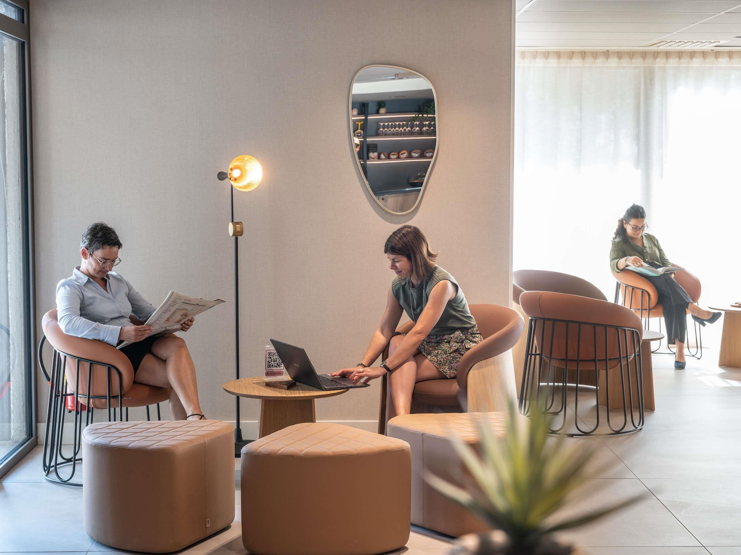 A modern lounge area with seating, a laptop on a table, and a wall-mounted mirror.