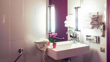 A modern bathroom with a white sink, a mirror, a hand dryer, a towel rack, and a potted orchid.