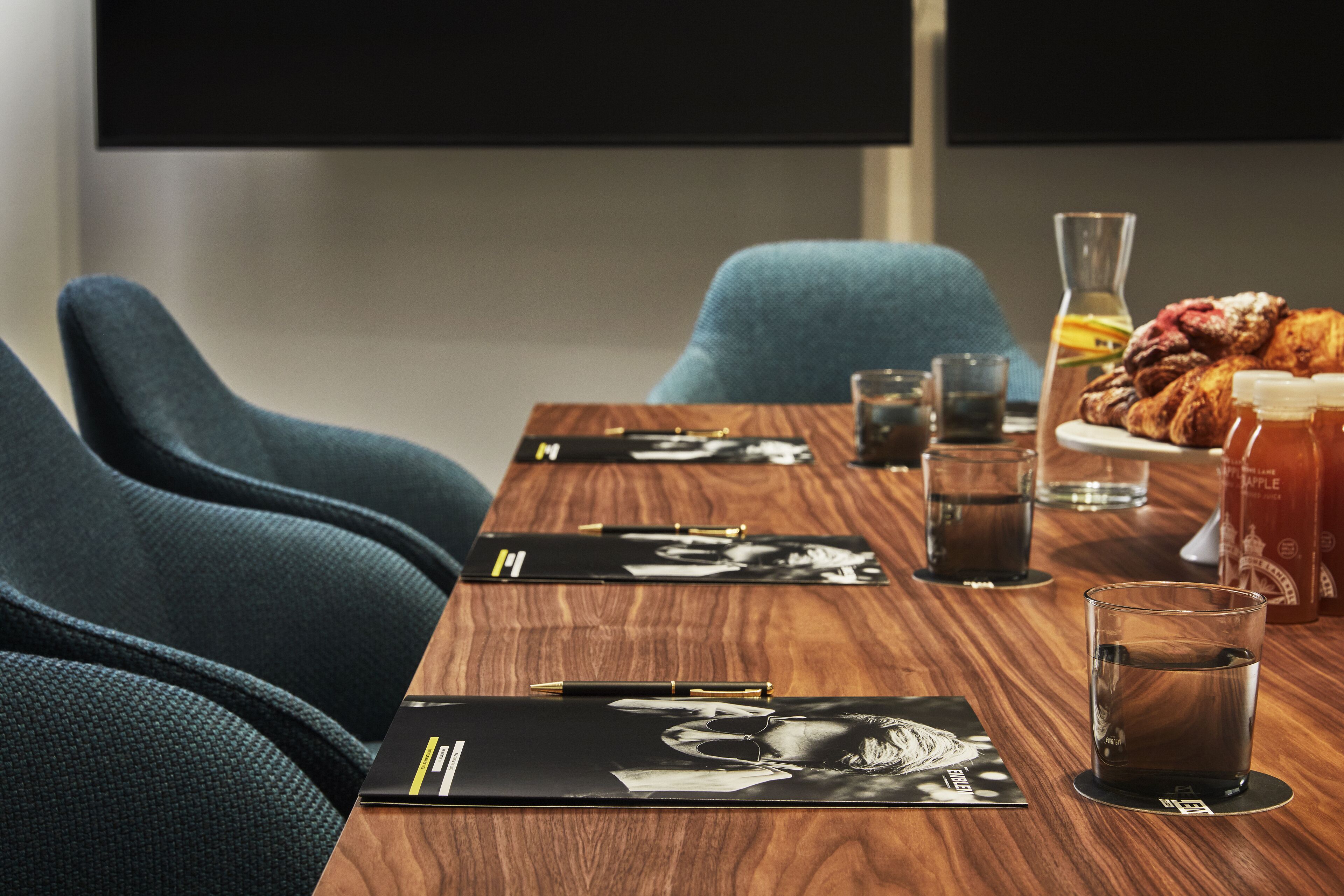 Une table de conférence avec des dossiers noirs, des stylos et des verres d’eau.