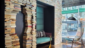 A cozy reading nook with a stack of books, a teal sofa, and a floor lamp. - Hotel Emblem San Francisco (San Francisco)
