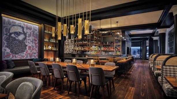 A modern bar area with a long wooden counter, multiple bar stools, and a variety of bottles and glasses. - Hotel Emblem San Francisco (San Francisco)