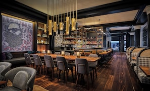 A modern bar area with a long wooden counter, multiple bar stools, and a variety of bottles and glasses.