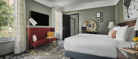 A hotel room with a large bed, a red sofa, a desk with a lamp, and a bulletin board.