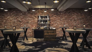 A bar area with a brick wall, multiple tables, and hanging lights.
