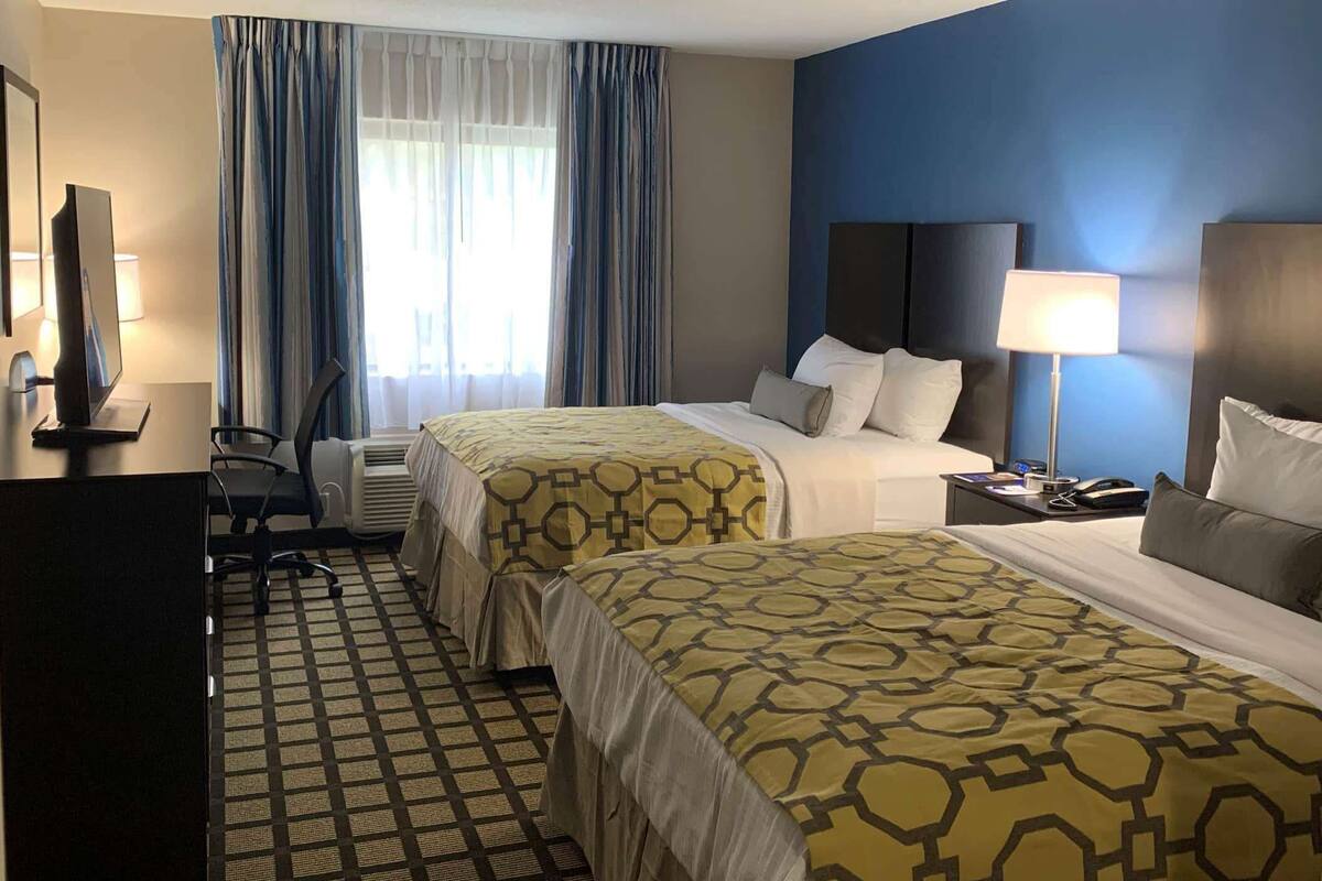 Ein Hotelzimmer mit zwei Betten, einem Schreibtisch mit Stuhl, einem Fernseher und einer Lampe.