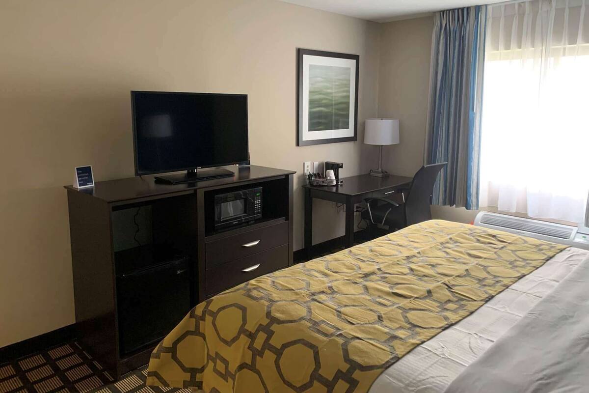 Ein Hotelzimmer mit einem Bett, einem Schreibtisch mit Computer, einem Fernseher, einer Mikrowelle und einer Kaffeemaschine.