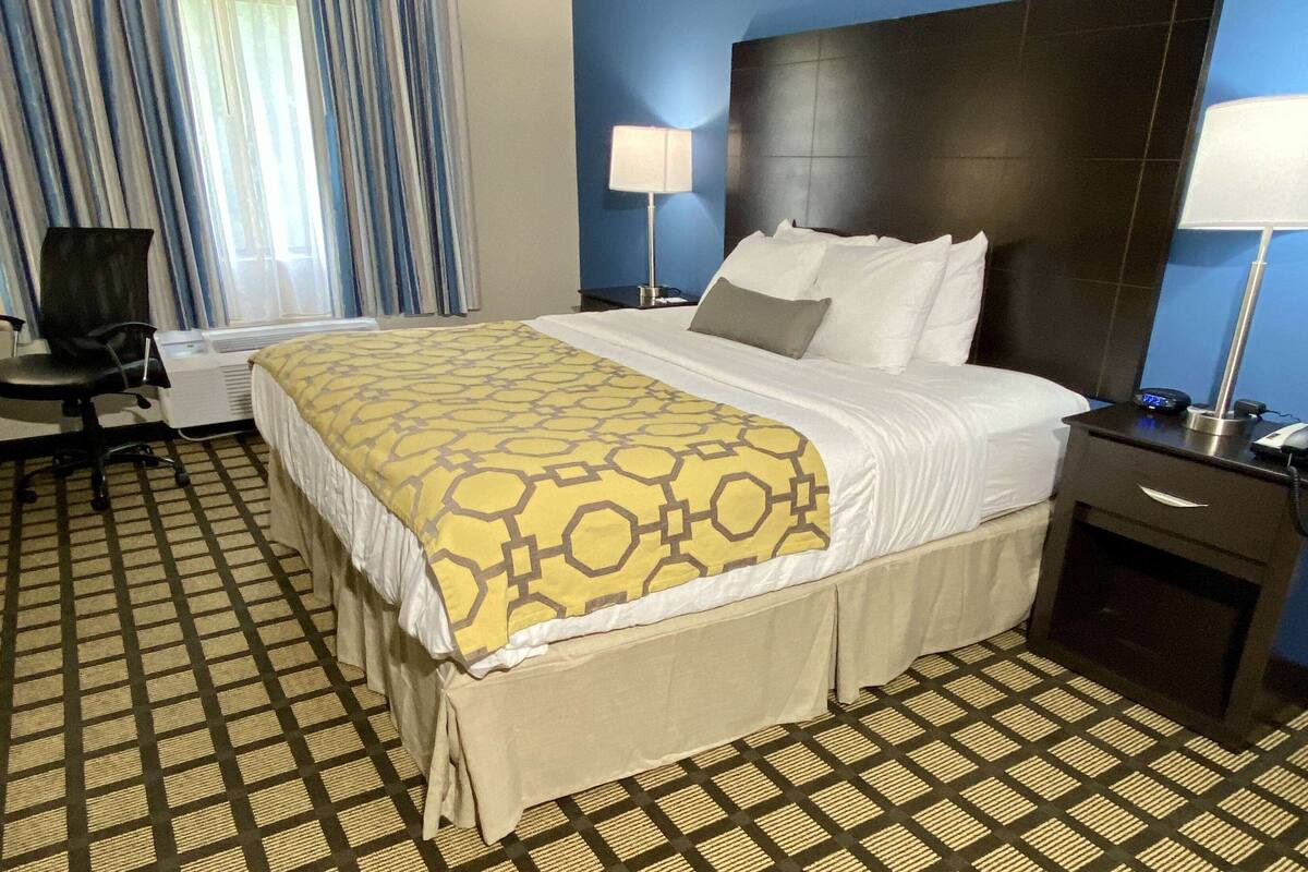 Ein Hotelzimmer mit einem großen Bett, einem Schreibtisch, einem Stuhl und einem fenster mit Vorhängen.