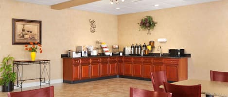 A hotel dining area with a kitchen counter, wooden cabinets, and a dining table with chairs.