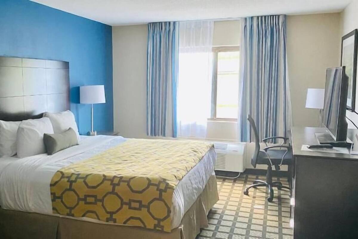 Ein Hotelzimmer mit Bett, Schreibtisch, Stuhl, Fernseher und einem Fenster mit Vorhängen.