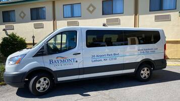 Un fourgon blanc de la chaîne Baymont Inn & Suites est garé devant un immeuble doté de nombreuses fenêtres et de plusieurs unités de climatisation.