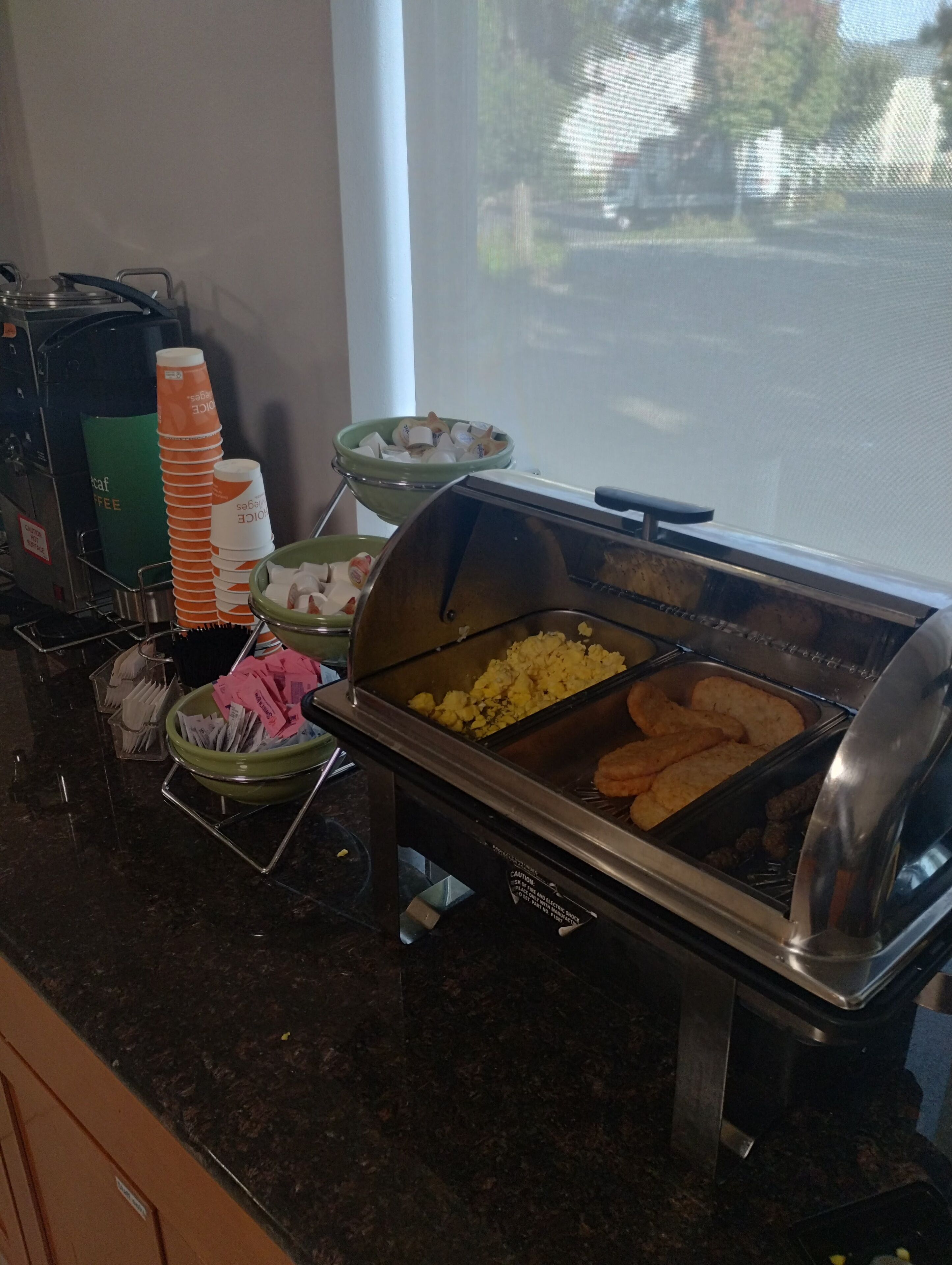 A buffet setup with various food items, including scrambled eggs and pastries, and a coffee station with disposable cups.