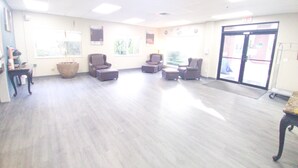 Um quarto espaçoso com uma grande janela, um balcão de recepção e várias áreas de estar com cadeiras e pufes.