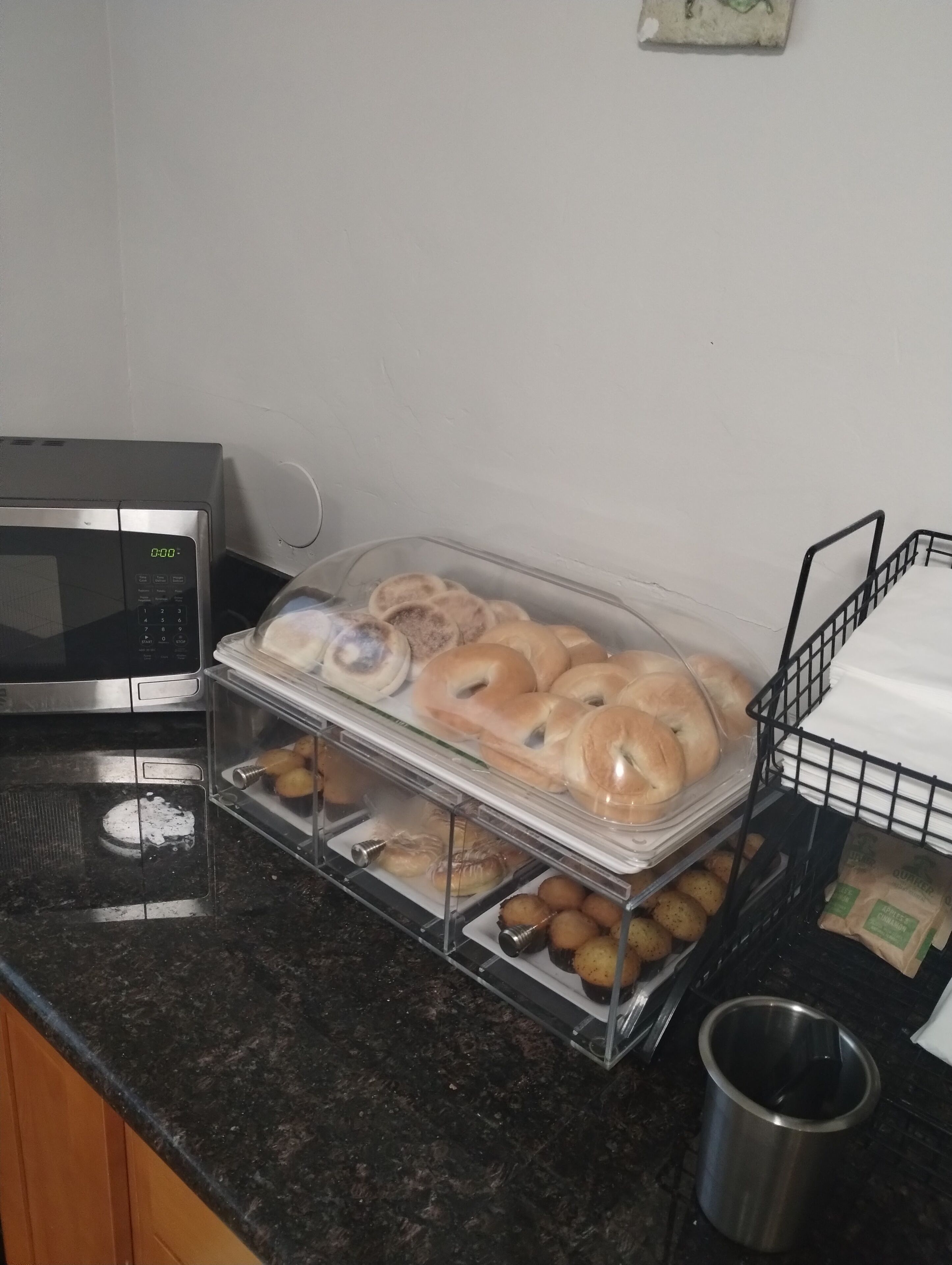 A kitchen counter with a microwave, a glass display case with pastries, and a metal basket.