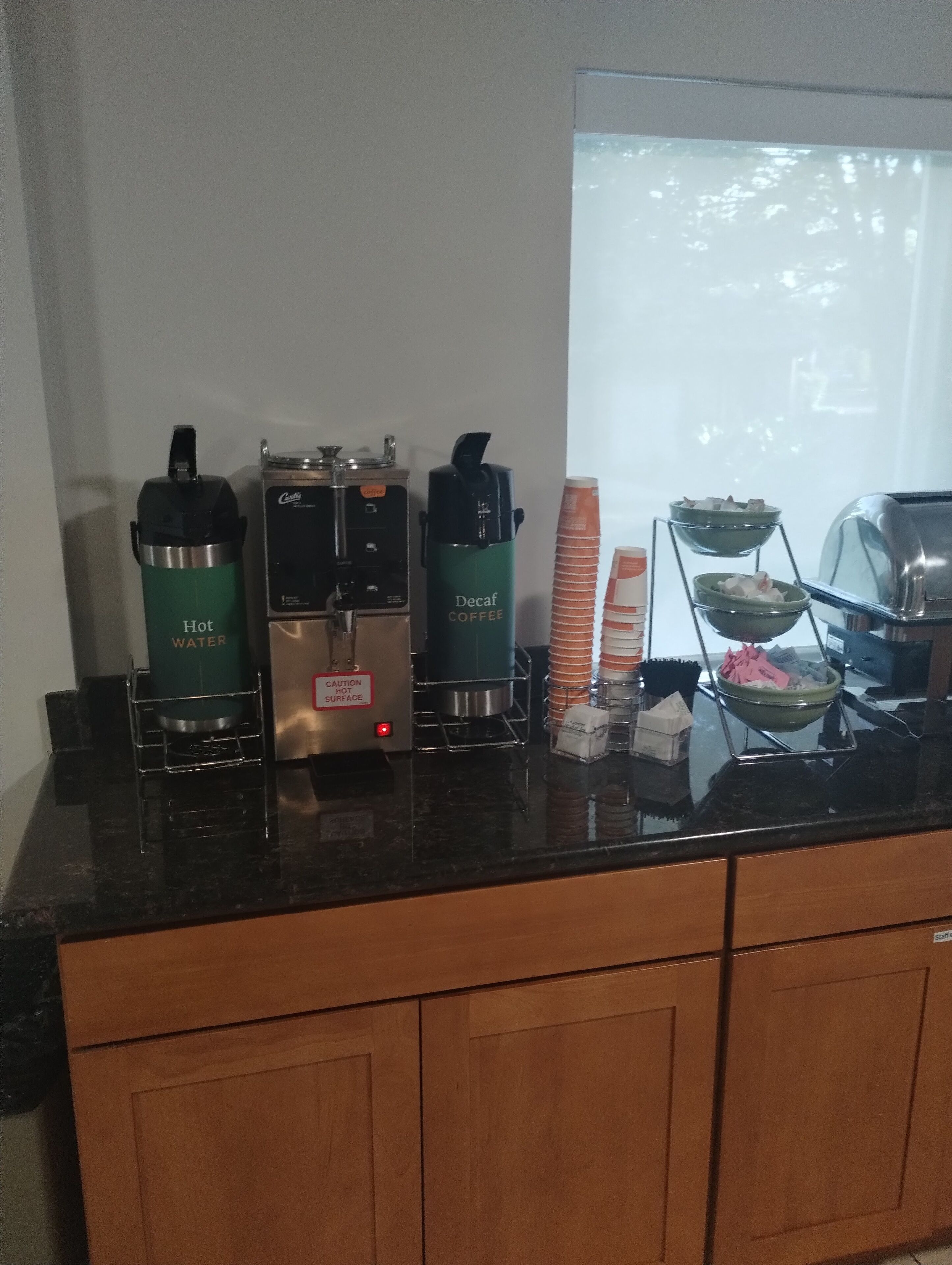 A coffee station with a coffee maker, a water dispenser, and a decaf coffee dispenser.
