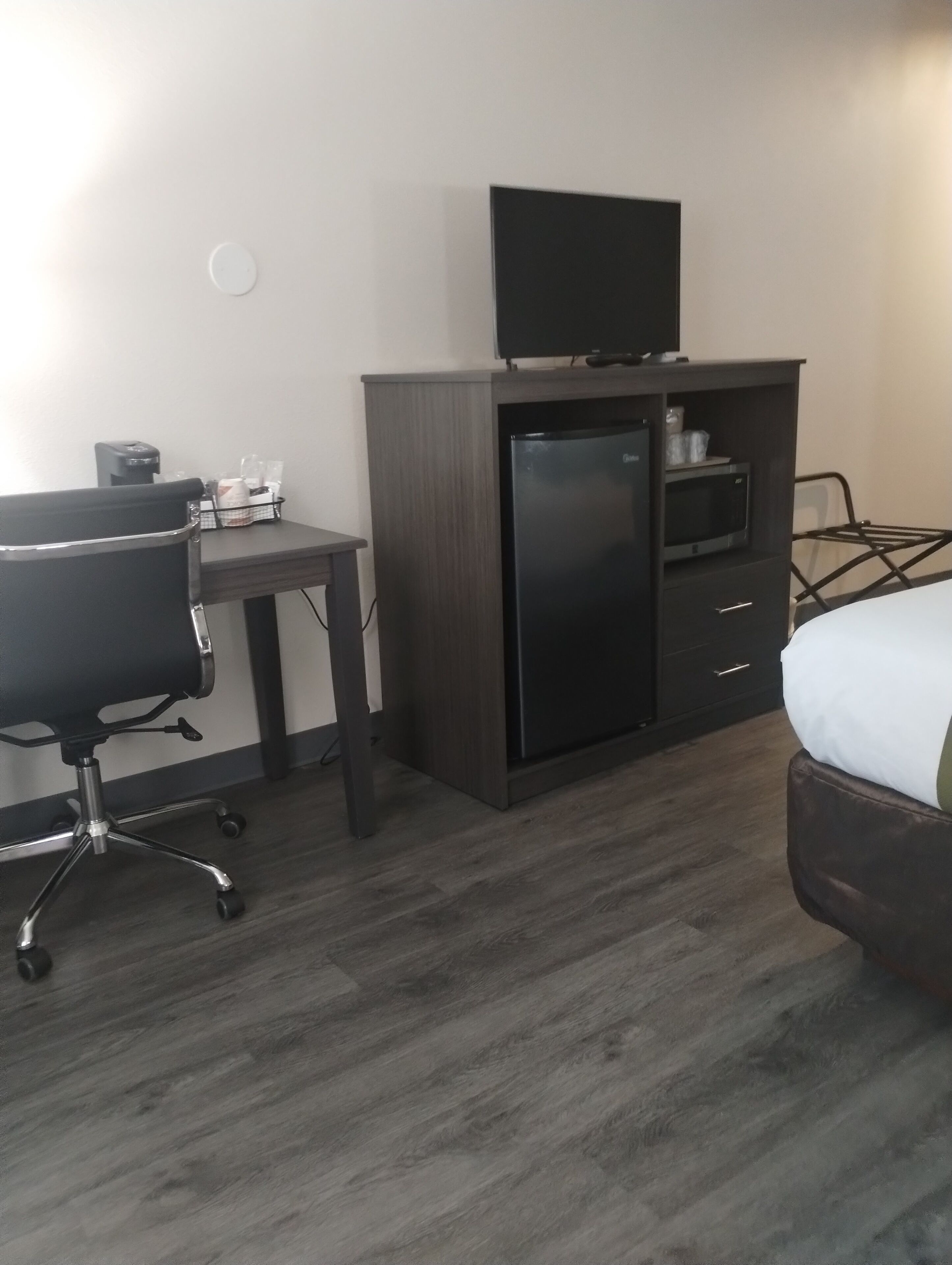 A hotel room with a bed, a desk with a chair, a minibar, and a television on a cabinet.