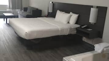 A hotel room with a bed, a sofa, a desk, a nightstand, a lamp, a phone, and a bathtub.