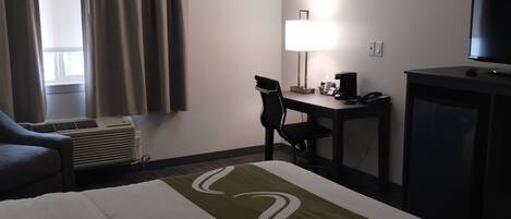 Habitación de hotel con cama, escritorio, silla, televisión y ventana con cortinas.