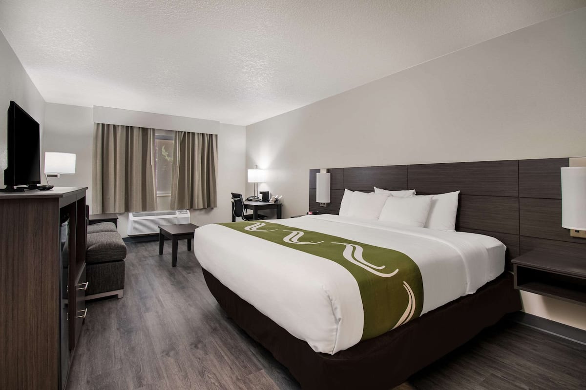 A hotel room with a large bed, a desk, a chair, a TV, and a window with curtains.