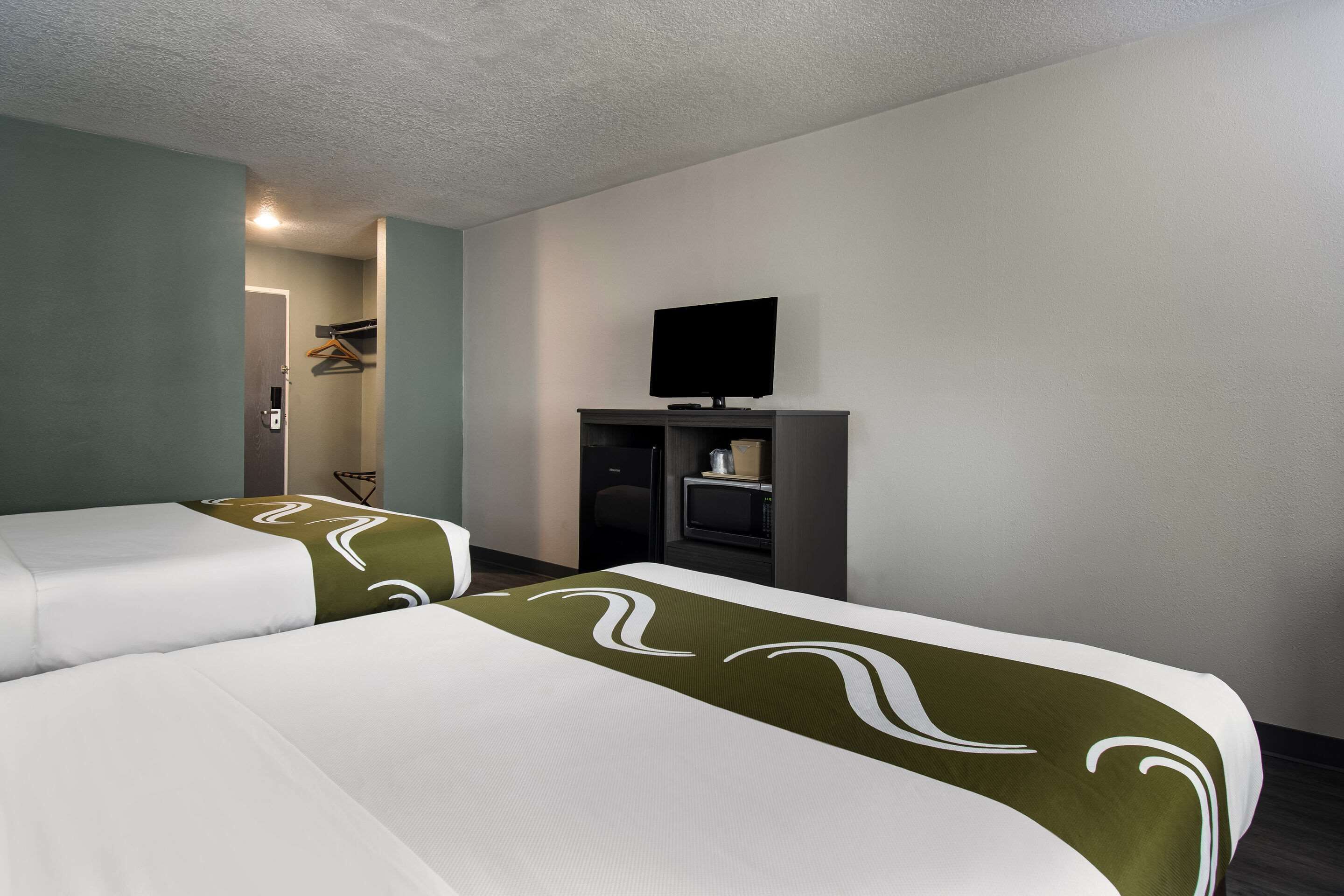 A hotel room with two beds, a television on a stand, and a door leading to a bathroom.