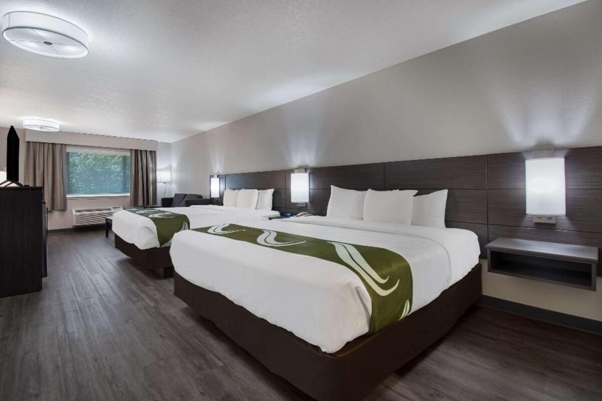 A hotel room with two beds, a desk, and a window.