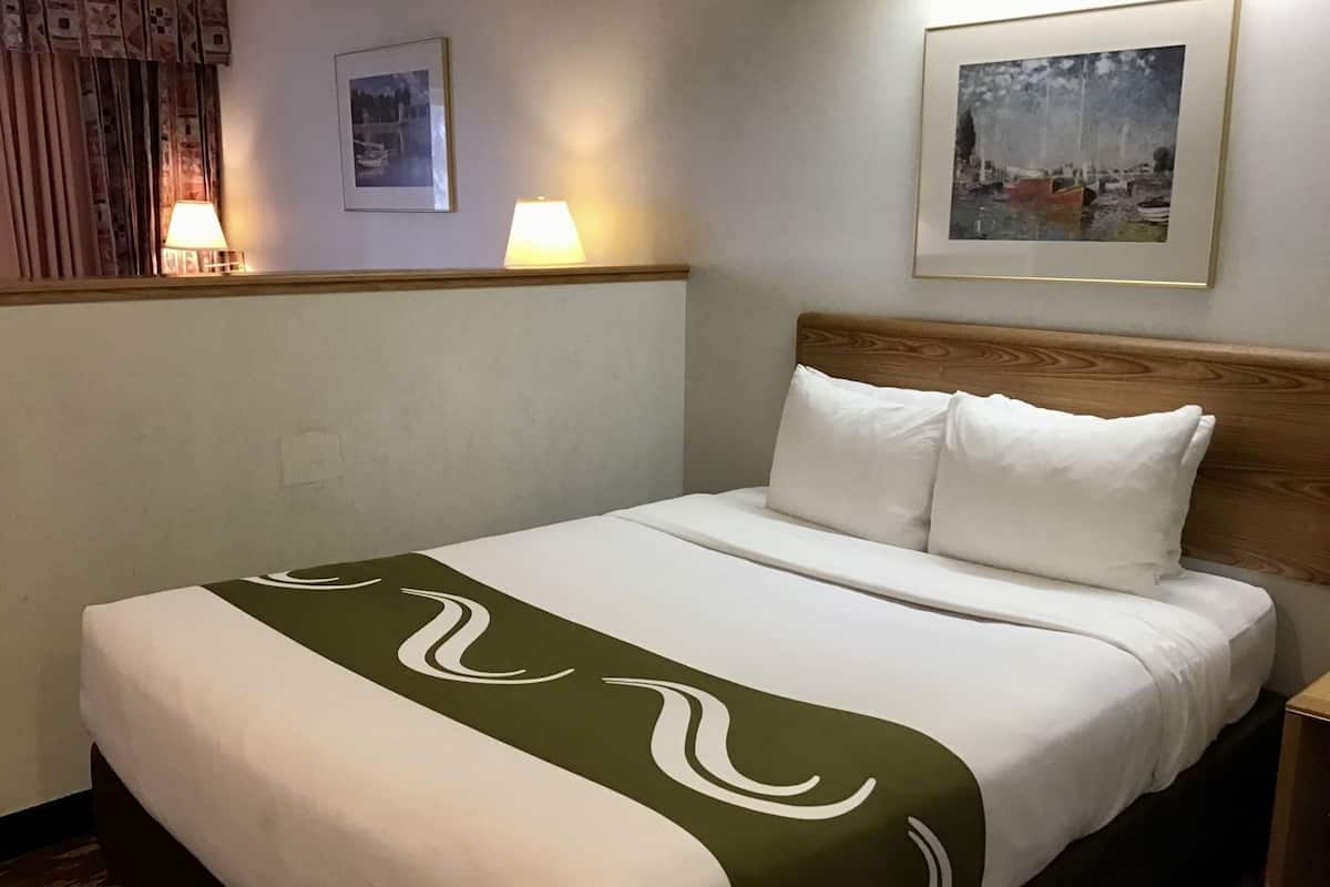A hotel room with a bed, two wall-mounted lamps, and two framed pictures.