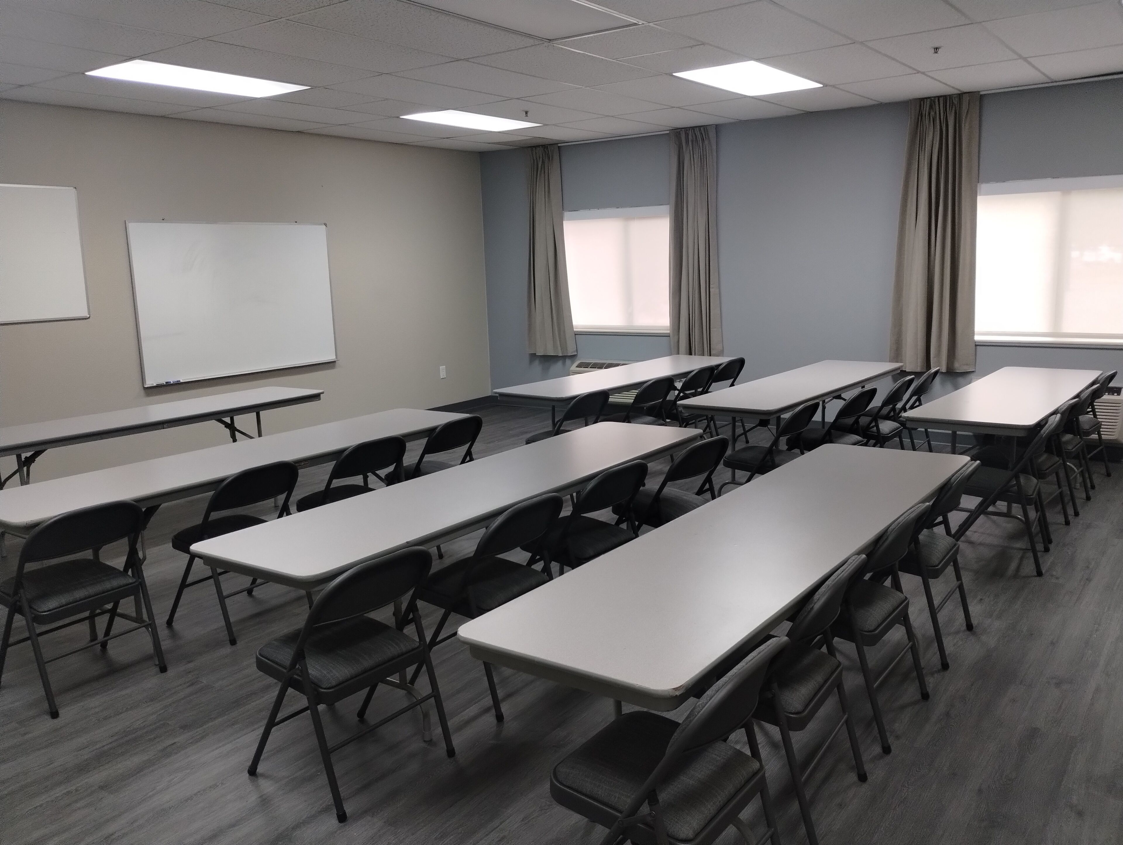 A conference room with multiple tables and chairs, a whiteboard, and large windows with curtains.