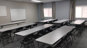 A conference room with multiple tables and chairs, a whiteboard, and large windows with curtains.