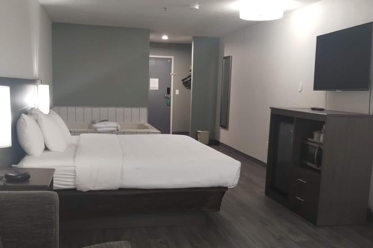 A hotel room with a bed, a desk, a chair, a TV, and a small cabinet.