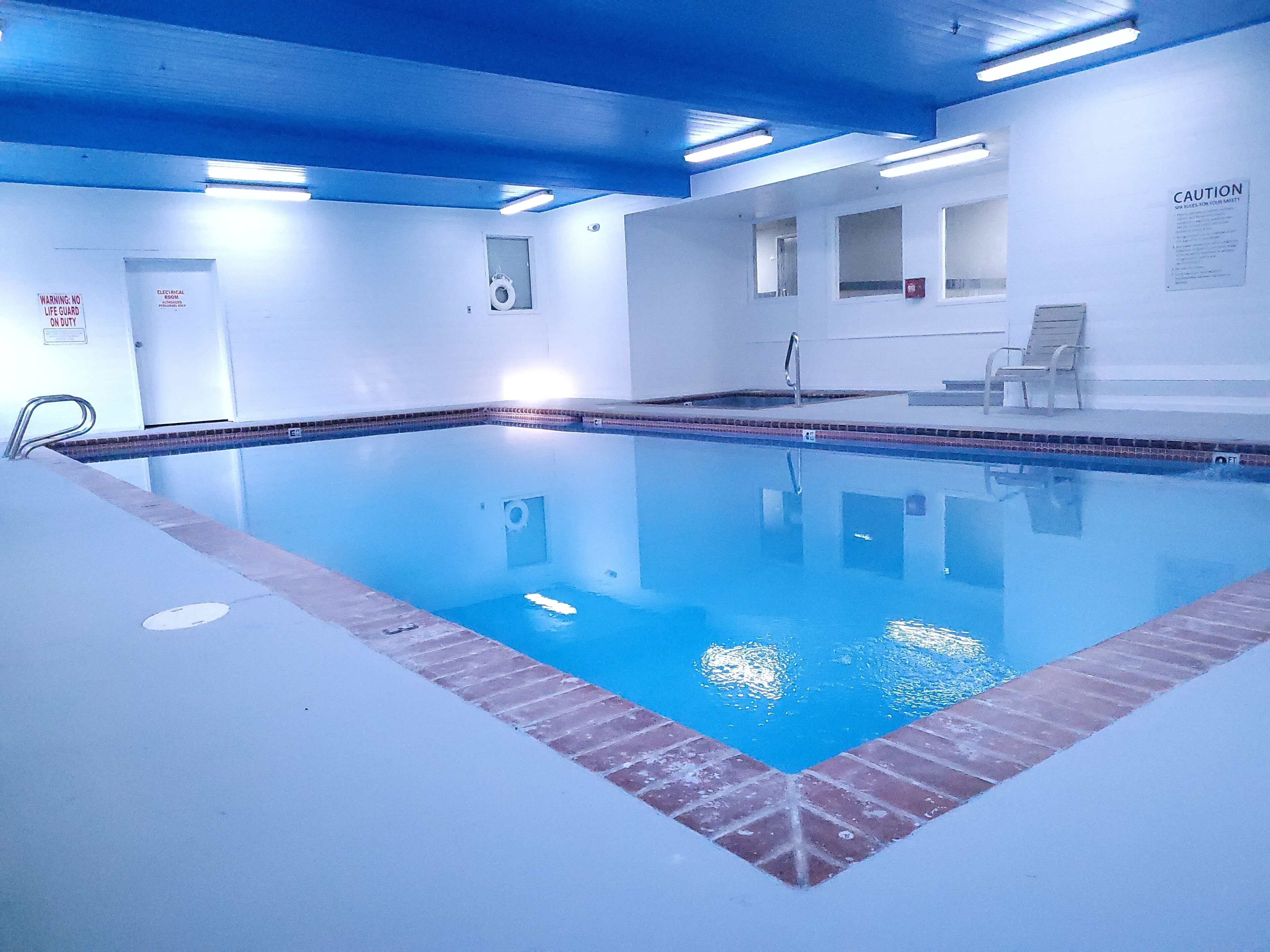 Una piscina con interni blu, circondata da muri bianchi e un cordone di mattoni rossi.