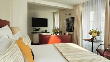 A hotel room with a bed, a desk, a television, and a small table with a vase of flowers.