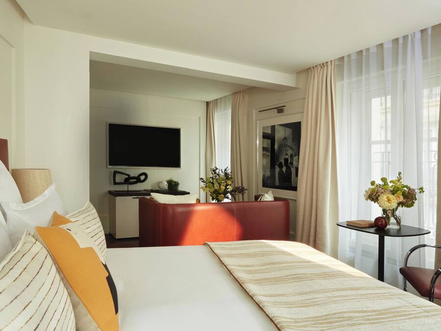 A hotel room with a bed, a desk, a television, and a small table with a vase of flowers.