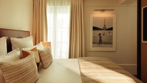 Habitación de hotel con una cama grande, cortinas color beige, un cuadro con la Torre Eiffel y un cabecero de madera.