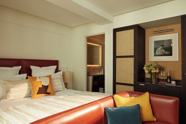 Habitación de hotel con una cama, un sofá de cuero rojo, un mueble de madera con espejo y un cuadro en la pared.