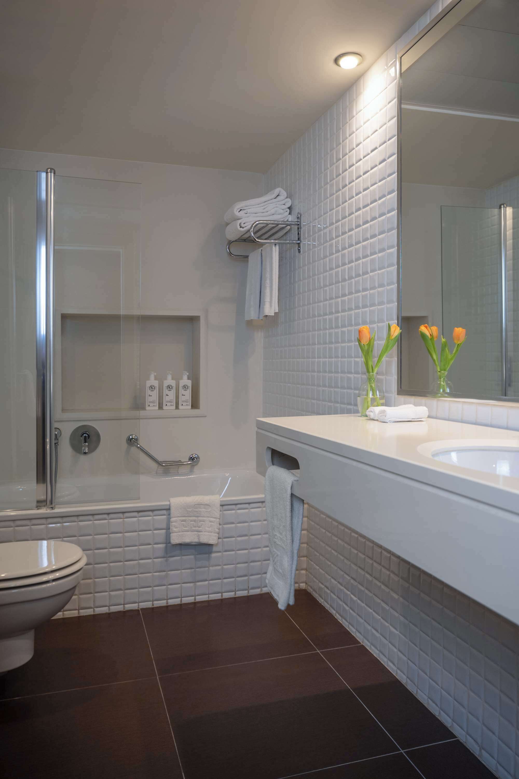 Un baño moderno con cabina de ducha de vidrio, lavamanos blanco y un espejo grande.